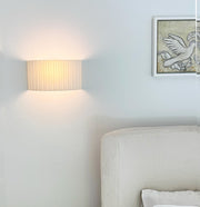 Light fixture on a wall next to a bed with a decorative pillow.